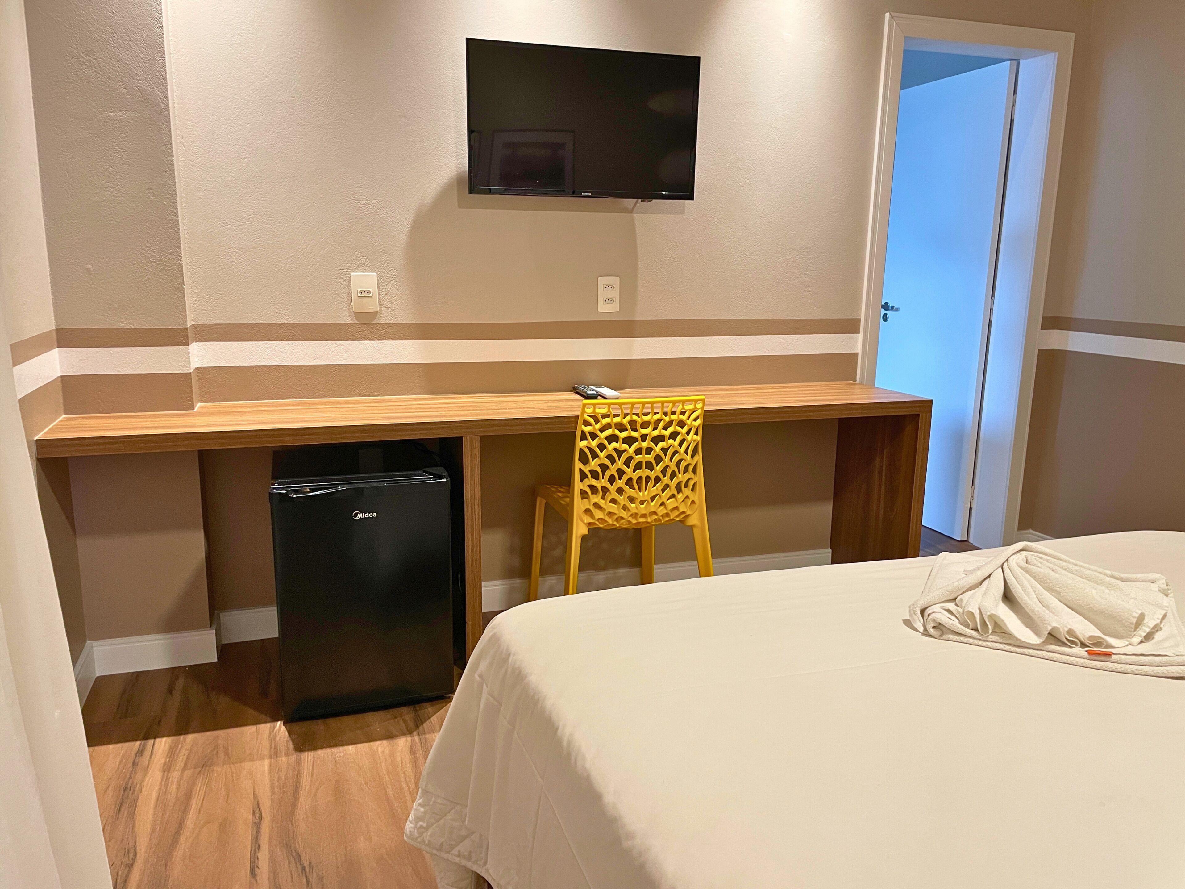 Una habitación de hotel con cama, escritorio con silla, televisor y minibar.