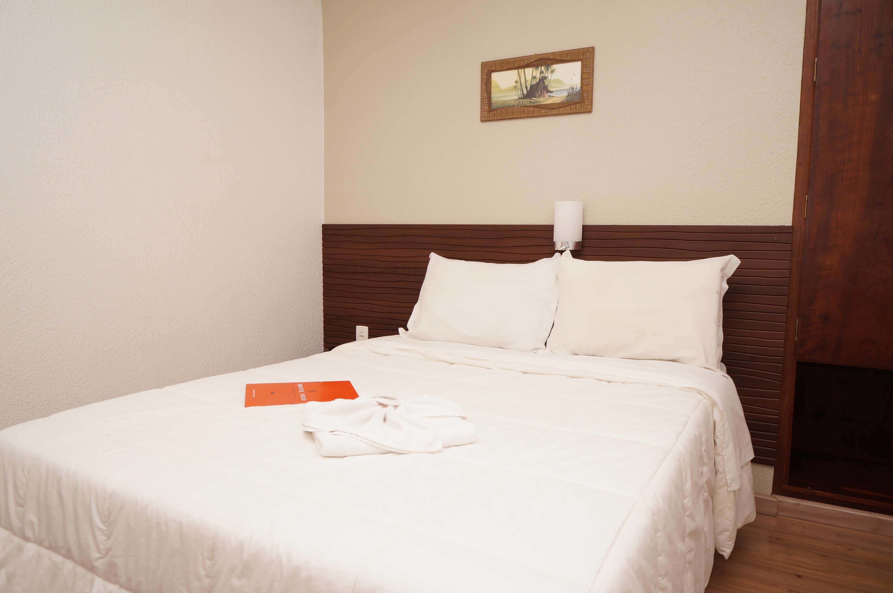 A neatly made bed with white bedding and a folded white robe on it.