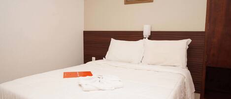 A neatly made bed with white bedding and a folded white robe on it.