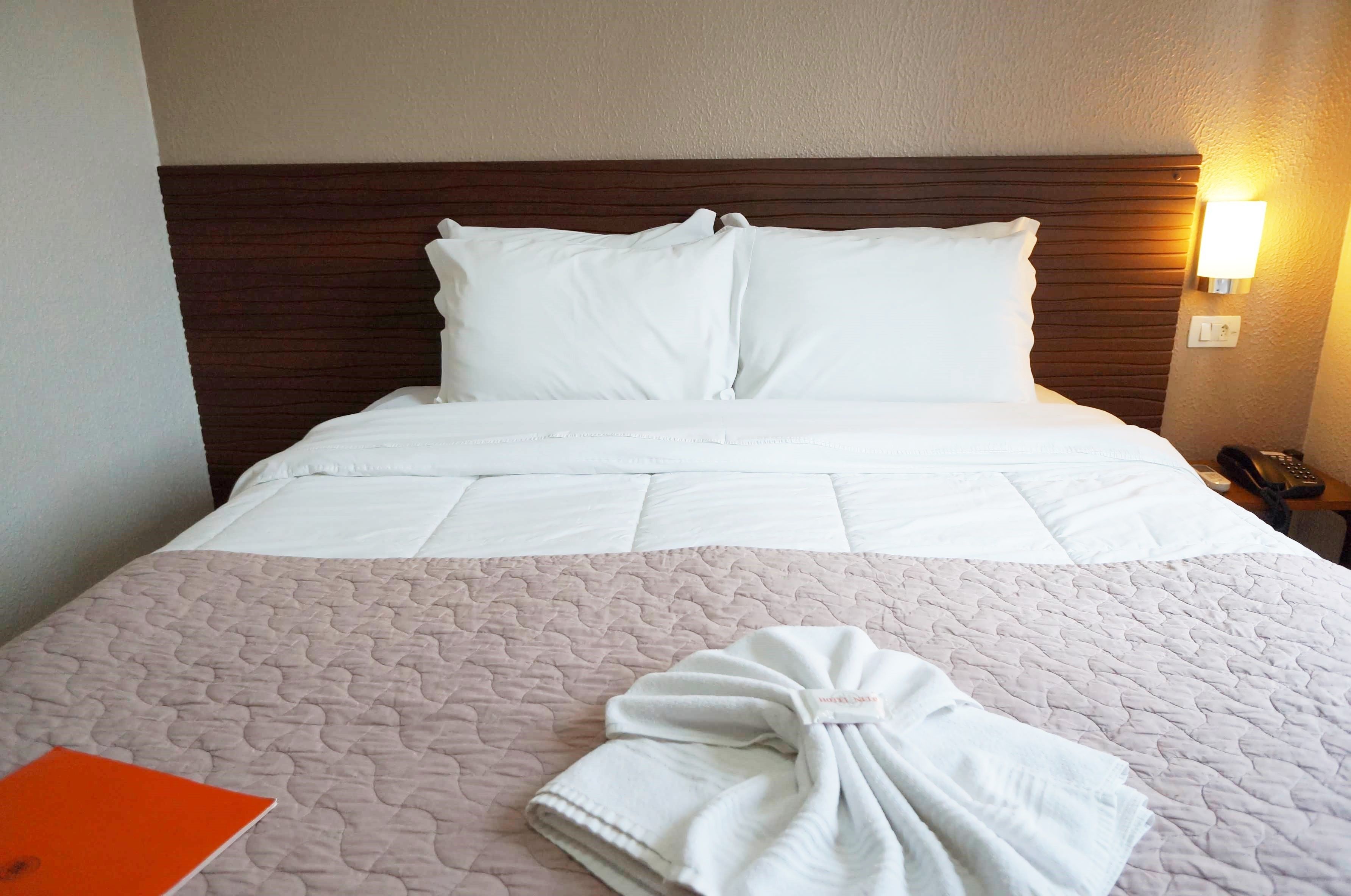 A neatly made bed with white linens and a pink quilted bedspread.