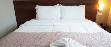 A neatly made bed with white linens and a pink quilted bedspread.