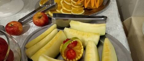 Una mesa de buffet con diversas frutas y verduras, entre ellas manzanas, plátanos y naranjas en rodajas.