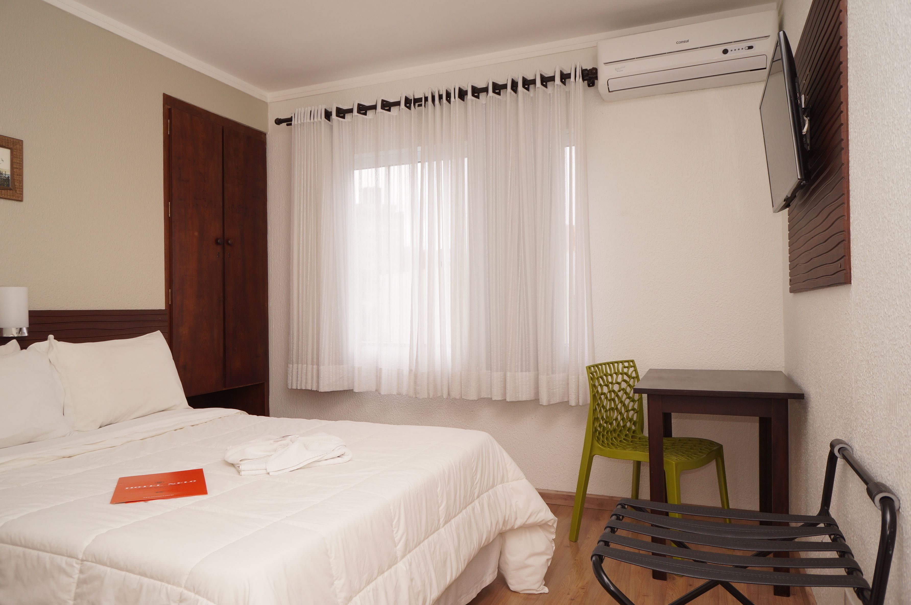 A hotel room with a bed, a desk, a chair, and a TV mounted on the wall.