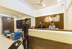 A hotel reception area with a wooden reception desk, a blue sofa, and a ceiling fan. - Galaxy Inn (Kolhapur)