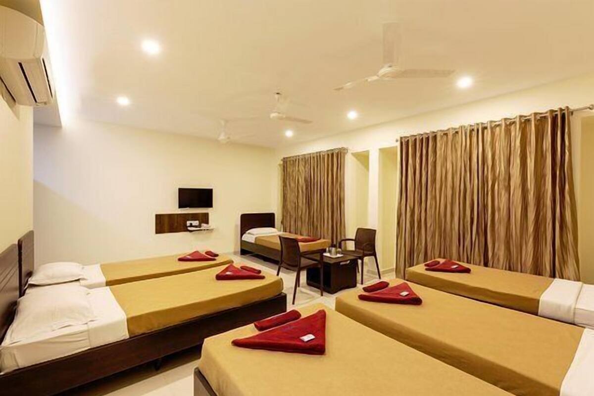 A hotel room with four single beds, a desk, a chair, and a TV on the wall.