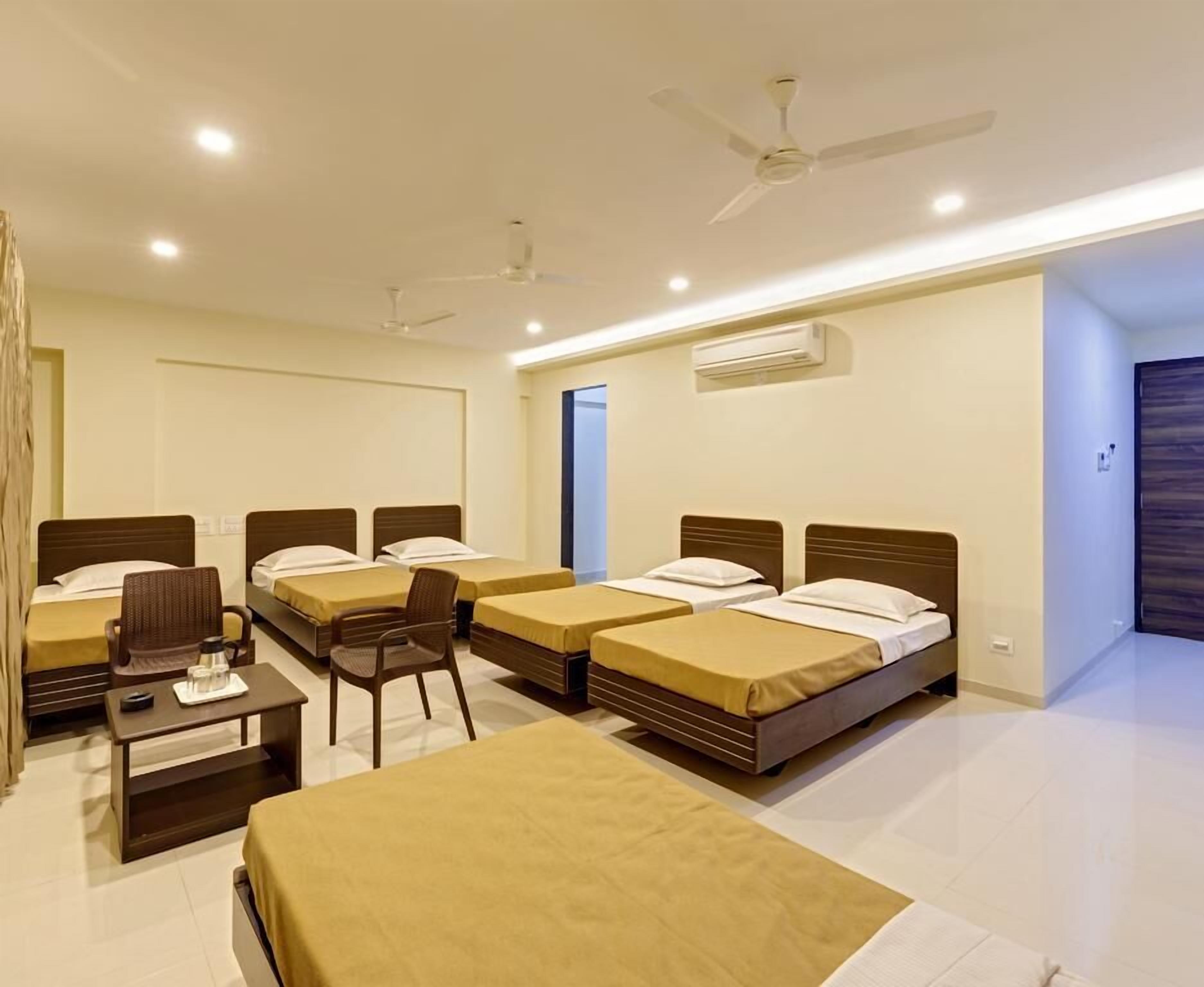 A hotel room with four single beds, a desk, a chair, and a ceiling fan.