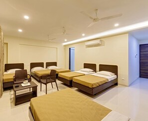 Habitación de hotel con cuatro camas individuales, un escritorio, una silla y un ventilador de techo.