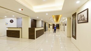 A hotel lobby with a reception desk, a person walking, and framed pictures on the walls. - Galaxy Inn (Kolhapur)