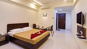 A modern hotel room with a large bed, a desk, chairs, a TV, and an air conditioning unit. - Galaxy Inn (Kolhapur)