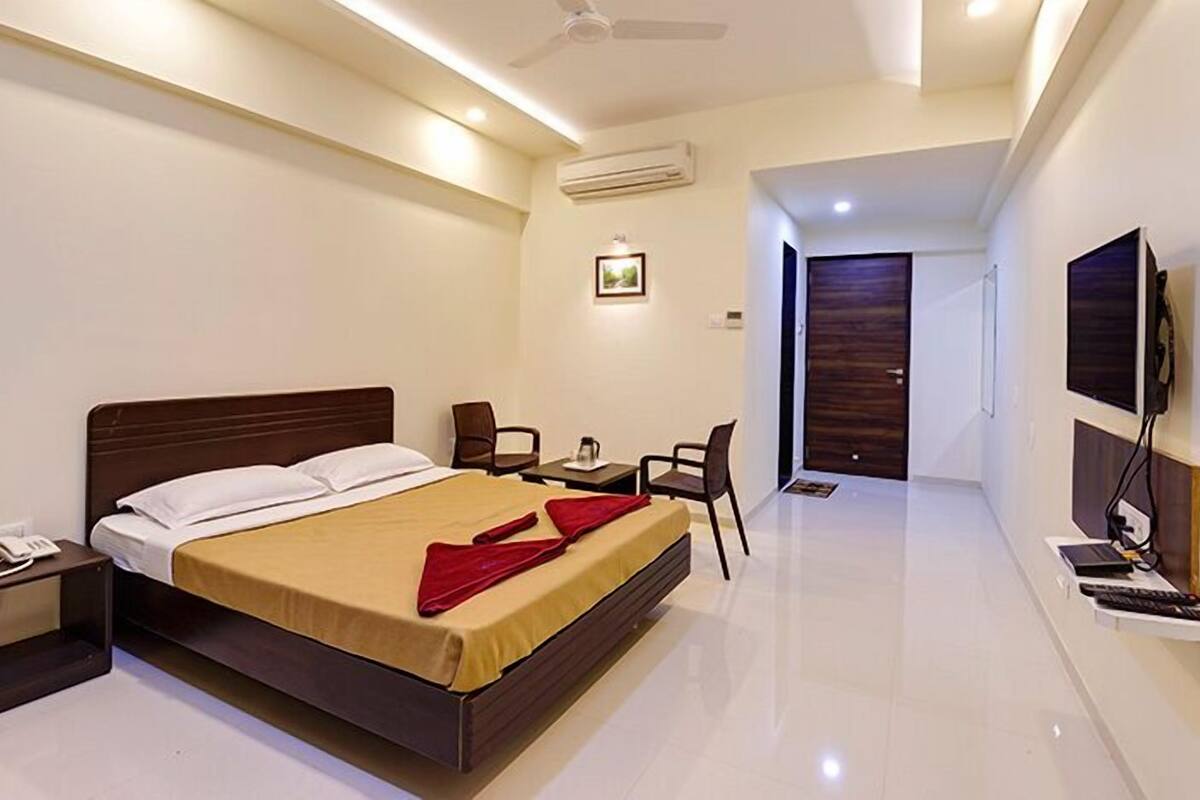 A modern hotel room with a large bed, a desk, chairs, a TV, and an air conditioning unit.