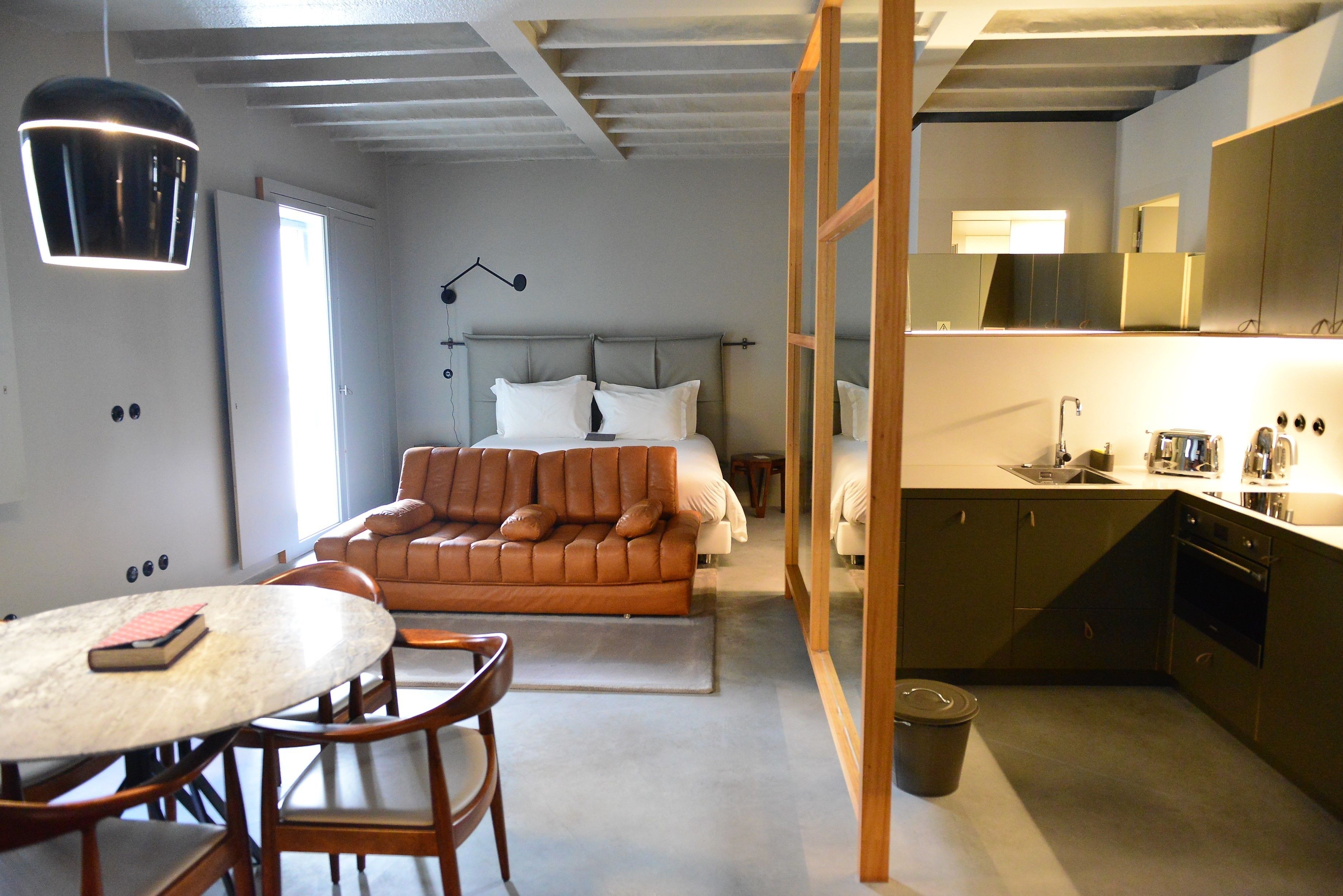 Una habitación de hotel compacta con cama, una pequeña mesa de comedor, un sofá, zona de cocina y baño.