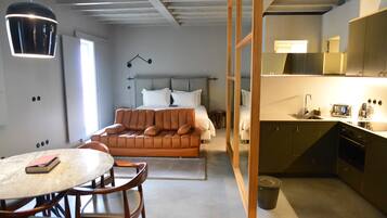 Una habitación de hotel compacta con cama, una pequeña mesa de comedor, un sofá, zona de cocina y baño.