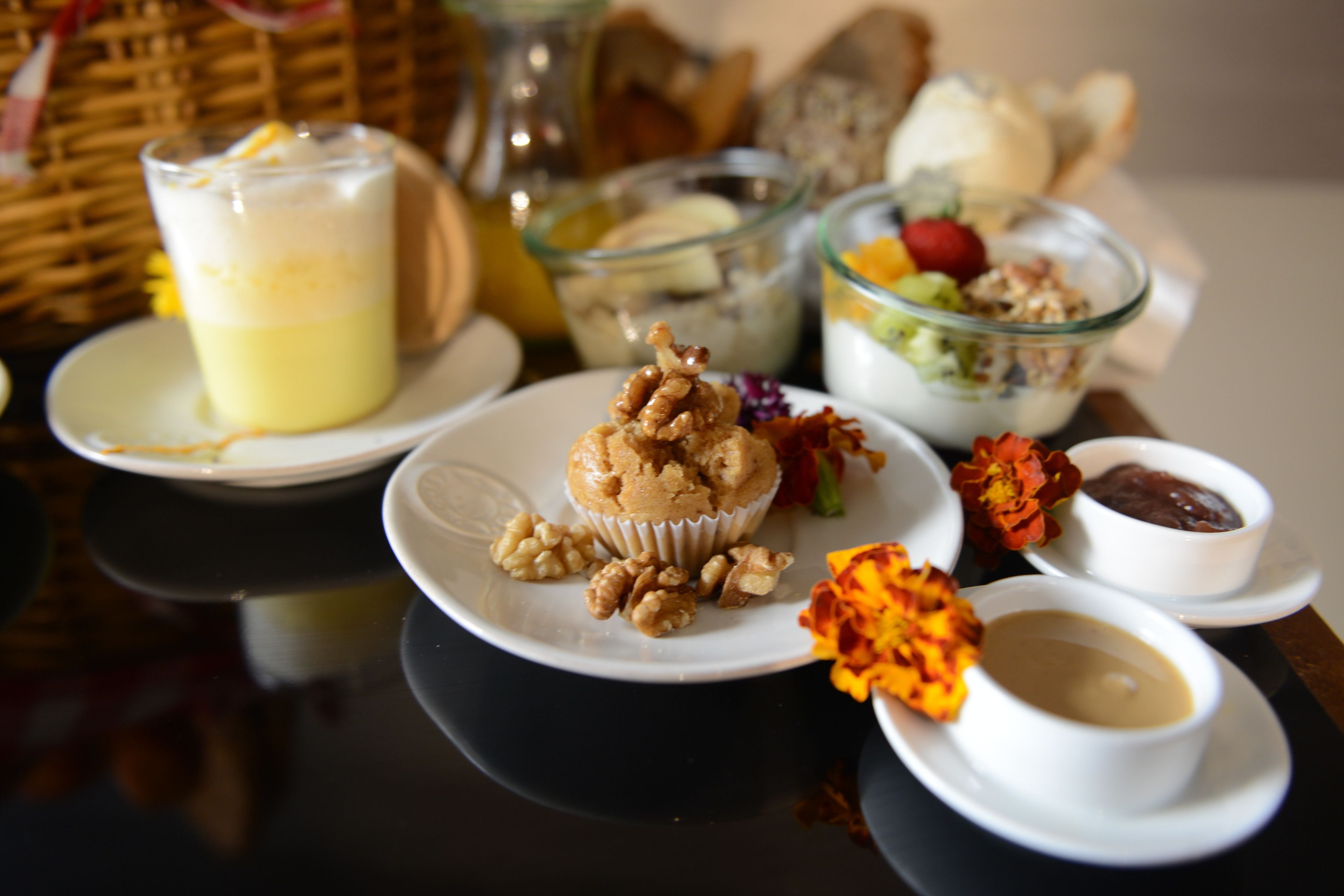 Uma mesa com diversos alimentos, incluindo um muffin, nozes, uma tigela de iogurte e um copo de uma bebida cremosa.