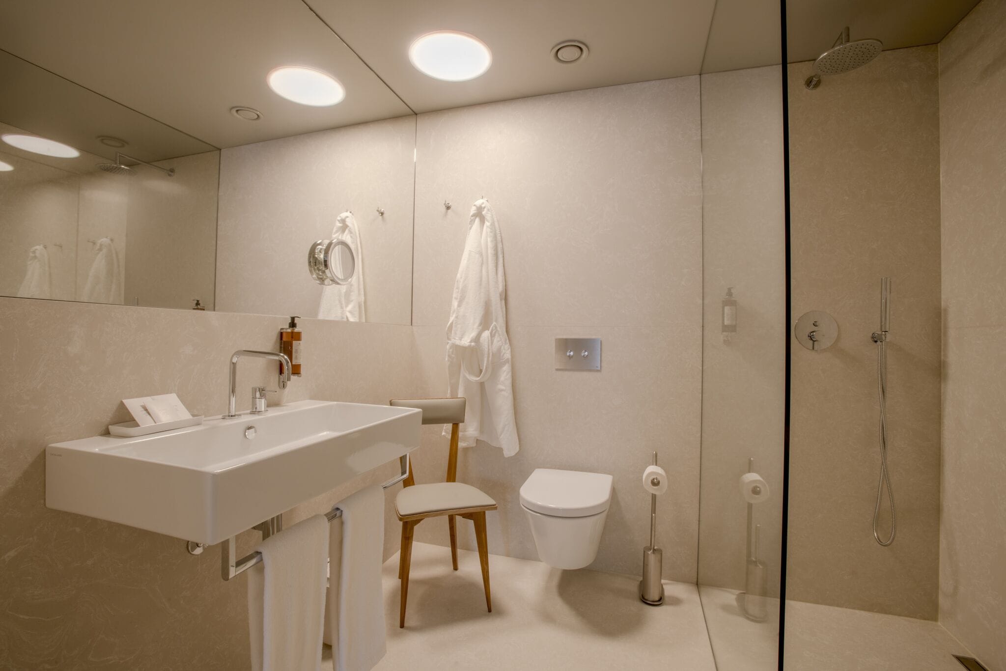 Un baño moderno con lavamanos, espejo, inodoro y ducha blancos.