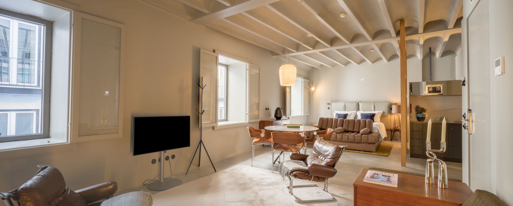 Un salon moderne doté d’un téléviseur à écran plat, de meubles en cuir, d’un coin repas et d’une cuisine en arrière-plan.