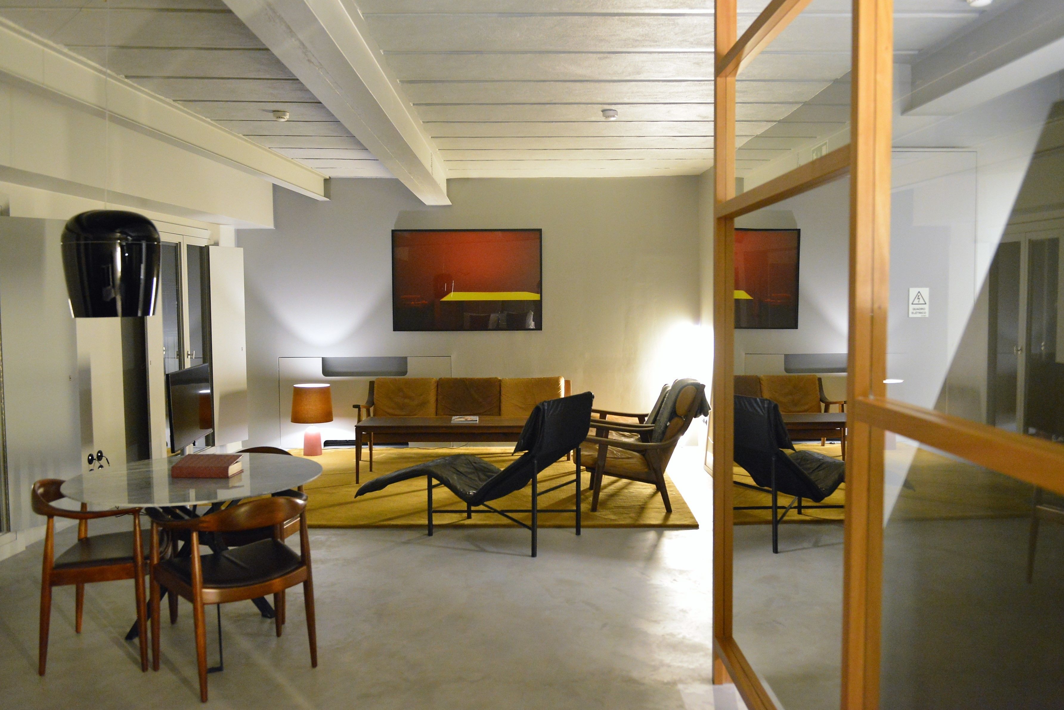 A modern living room with a glass table, wooden chairs, a sofa, and a large abstract painting on the wall.