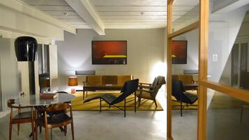 A modern living room with a glass table, wooden chairs, a sofa, and a large abstract painting on the wall.