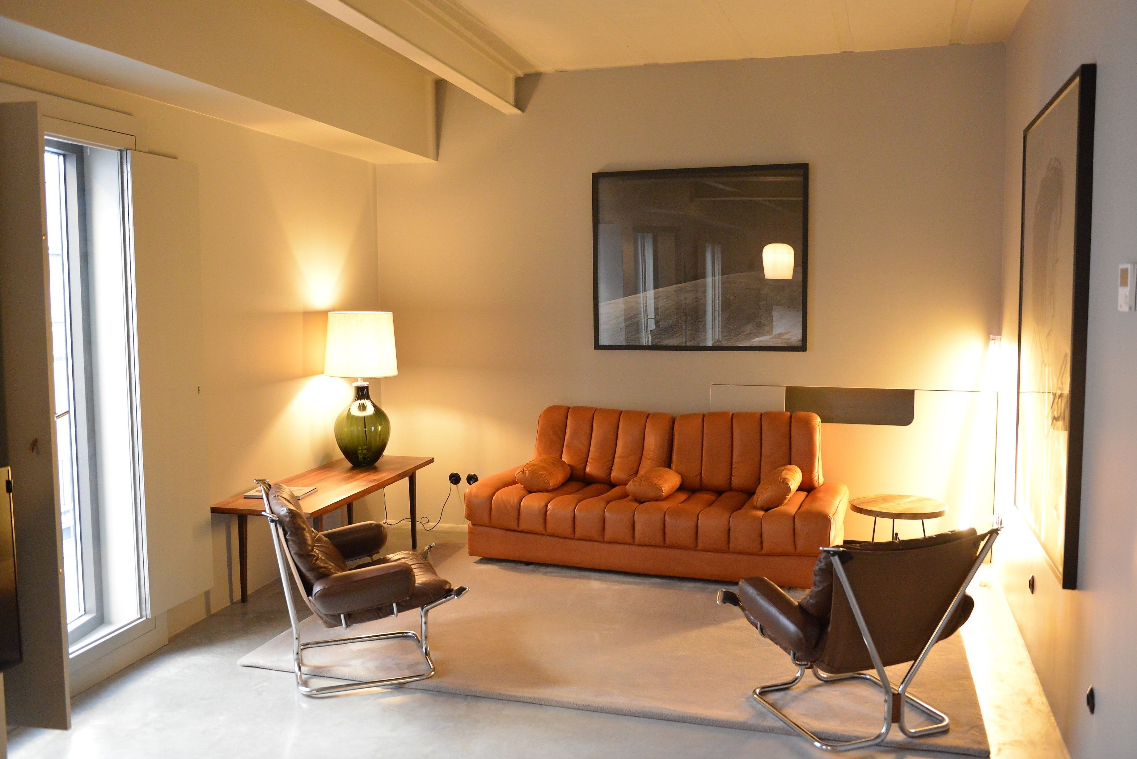 Una sala de estar moderna con un sofá de cuero, dos sillones, una mesita y una lámpara.