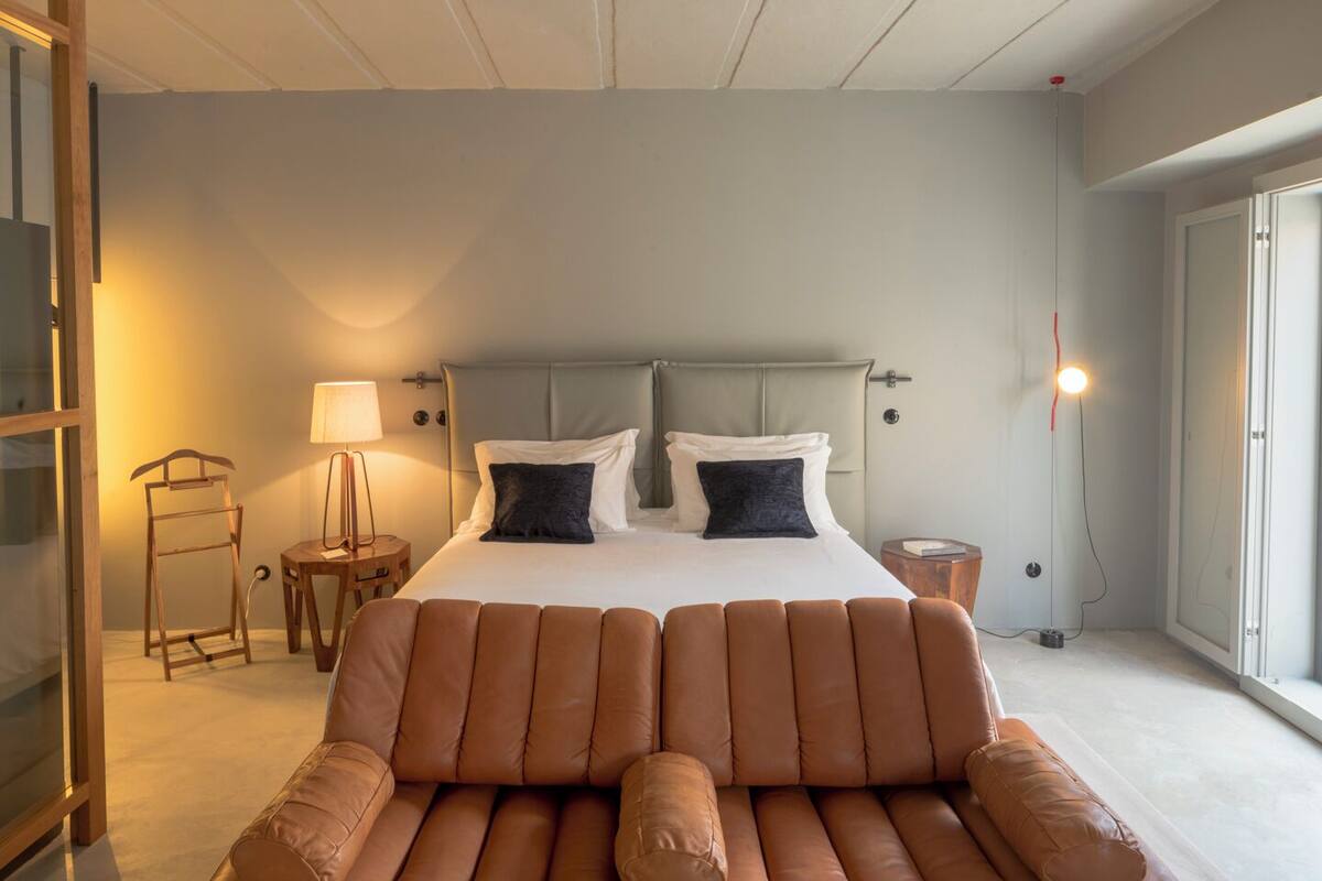 Une chambre à coucher moderne avec un grand lit, un canapé en cuir, une table de chevet, une lampe et une fenêtre.