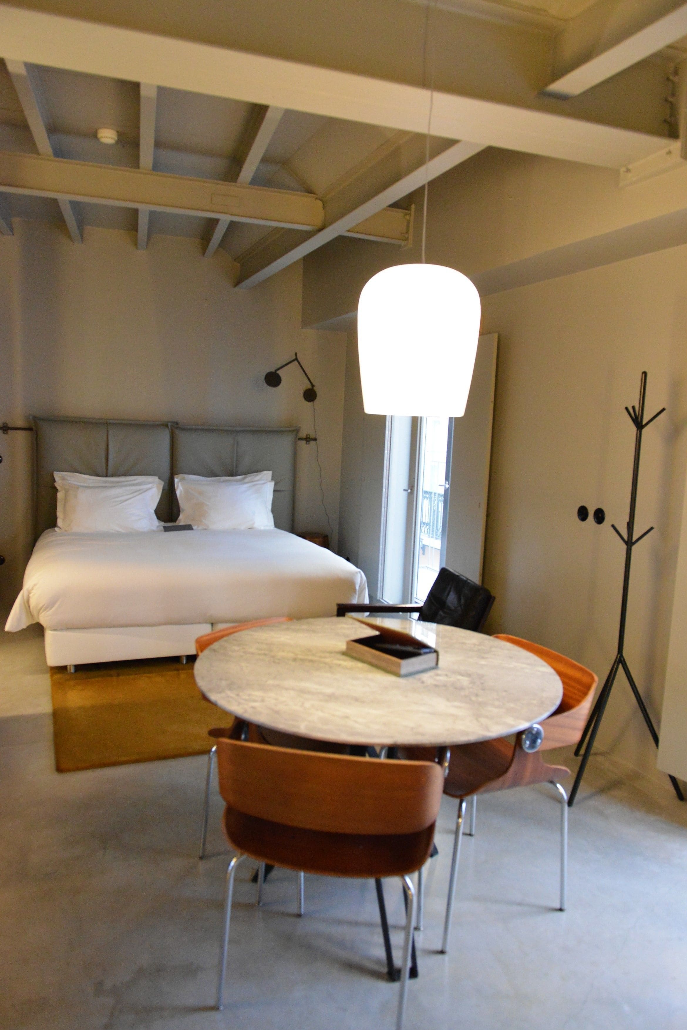 A modern bedroom with a large bed, a round dining table with chairs, and a floor lamp.