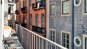 Une rue étroite en milieu urbain, bordée d’immeubles à plusieurs étages, de balcons et dotée d’un petit espace extérieur aménagé en terrasse.