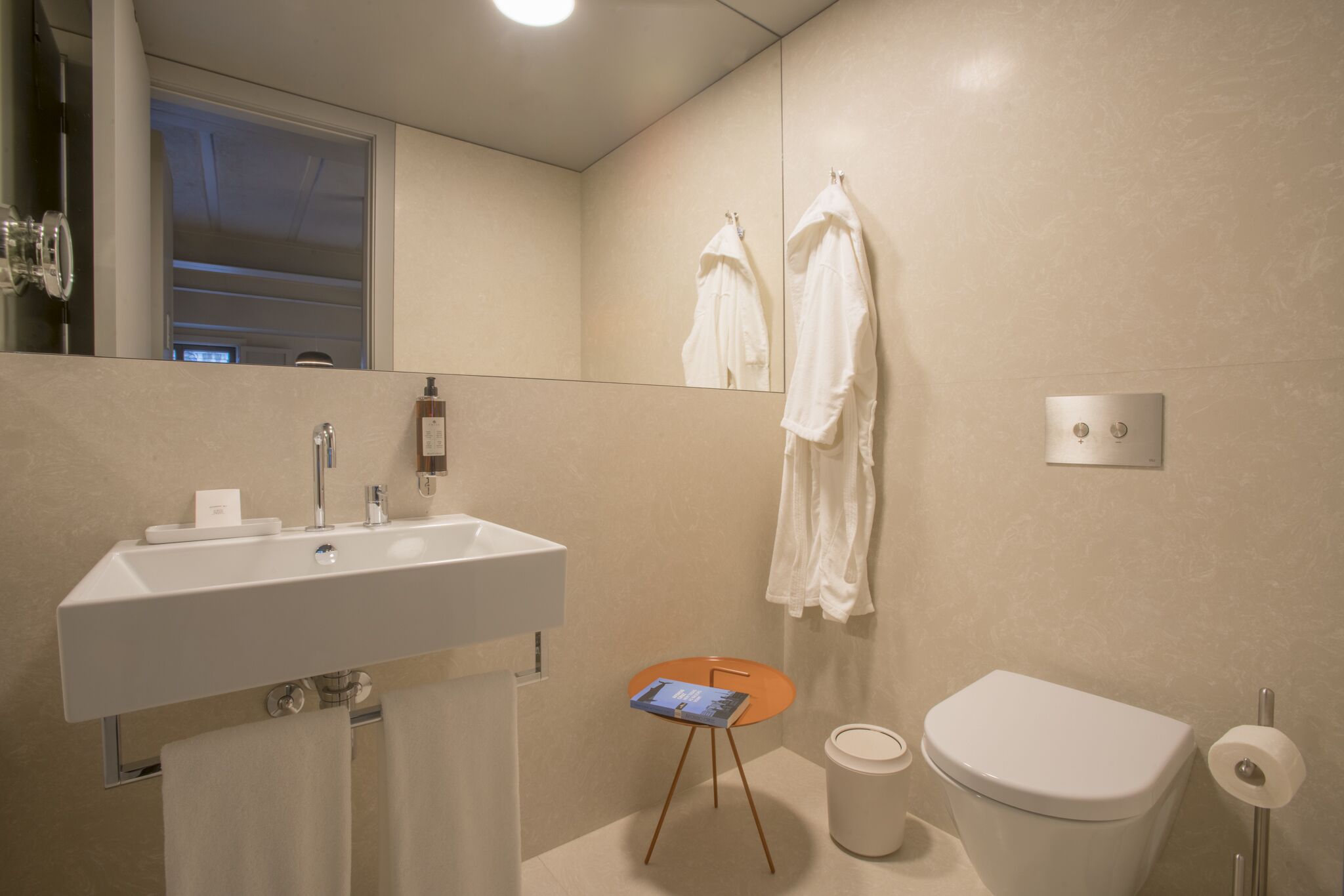 A modern bathroom with a white sink, a toilet, and a small table with a book.