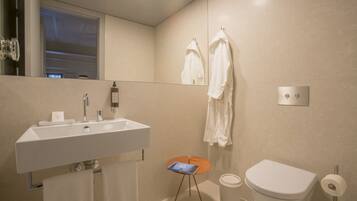 A modern bathroom with a white sink, a toilet, and a small table with a book.