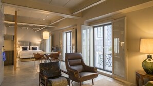 Une chambre d’hôtel spacieuse comprenant un lit, un coin repas, un fauteuil et un balcon avec vue.