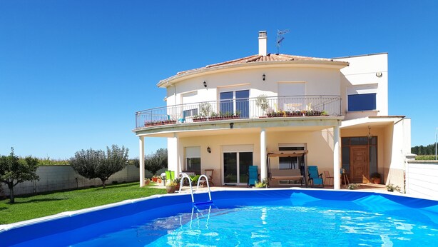 Ein zweistöckiges Haus mit Swimmingpool, überdachter Terrasse und einem Balkon mit Pflanzen.