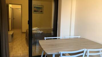 A room with a wooden table and white chairs, a glass door leading to a bathroom, and a painting on the wall.
