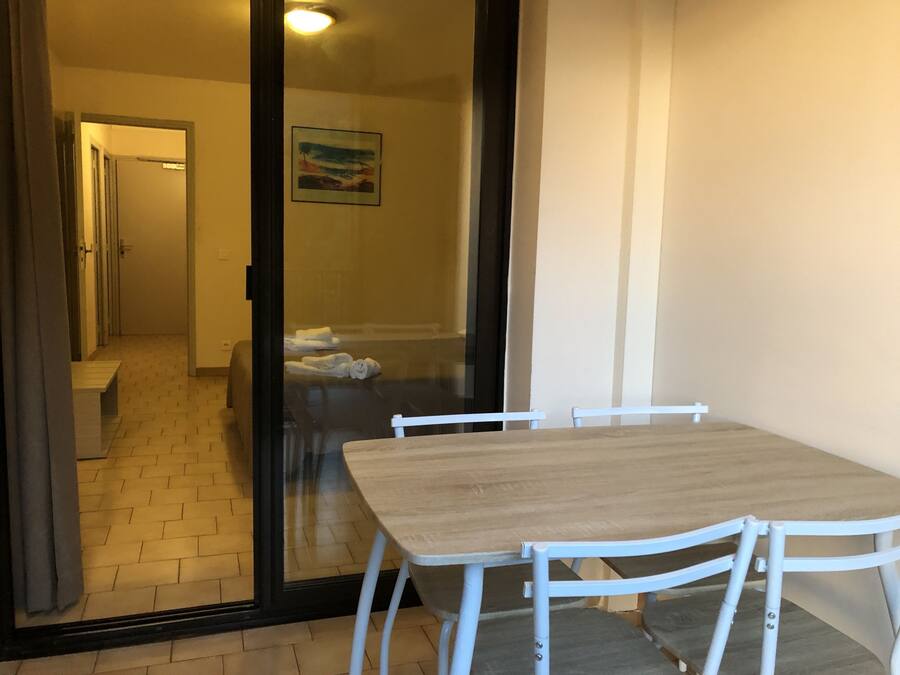 A room with a wooden table and white chairs, a glass door leading to a bathroom, and a painting on the wall.