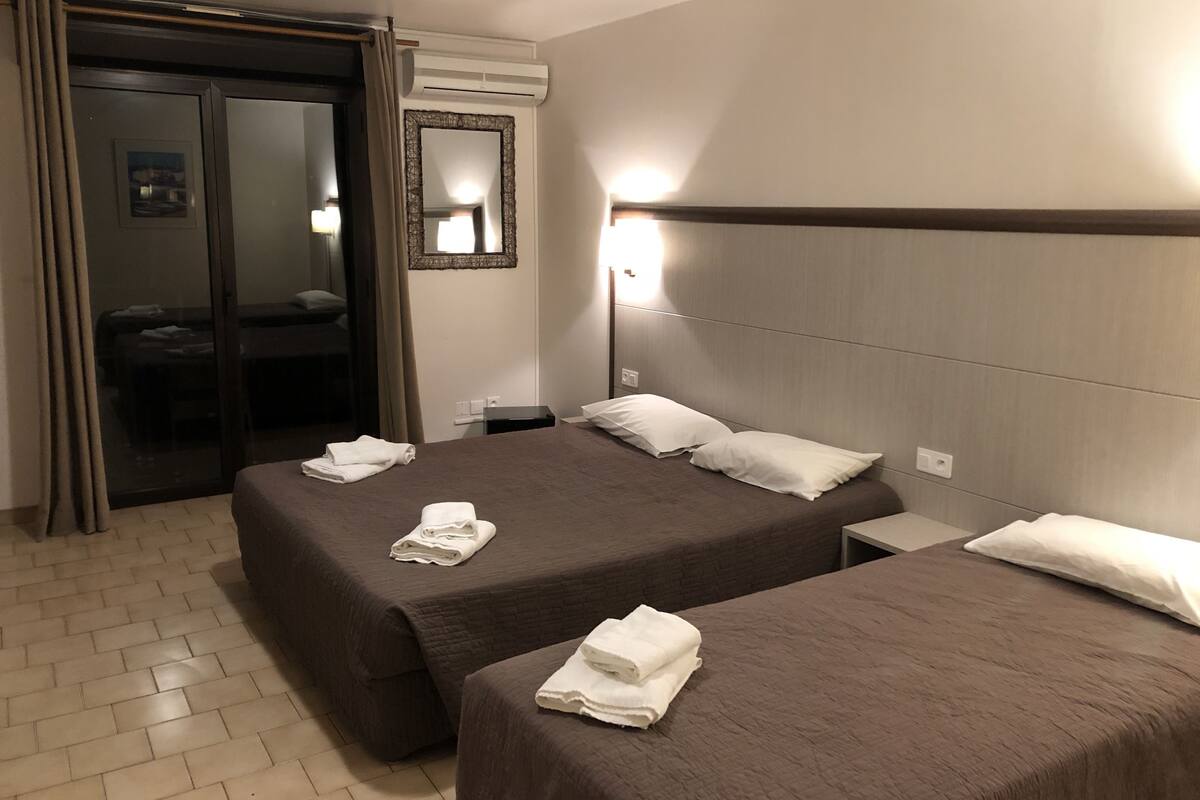 A hotel room with two beds, a mirror, an air conditioning unit, and a door leading to a bathroom.