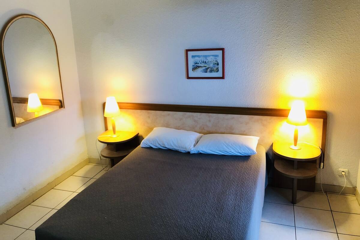 A hotel room with a bed, two bedside lamps, a mirror, and a framed picture on the wall.