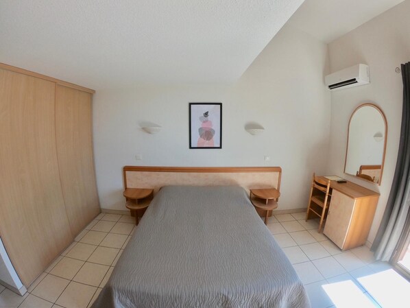 Un dormitorio con cama, escritorio, silla, armario y unidad de aire acondicionado.
