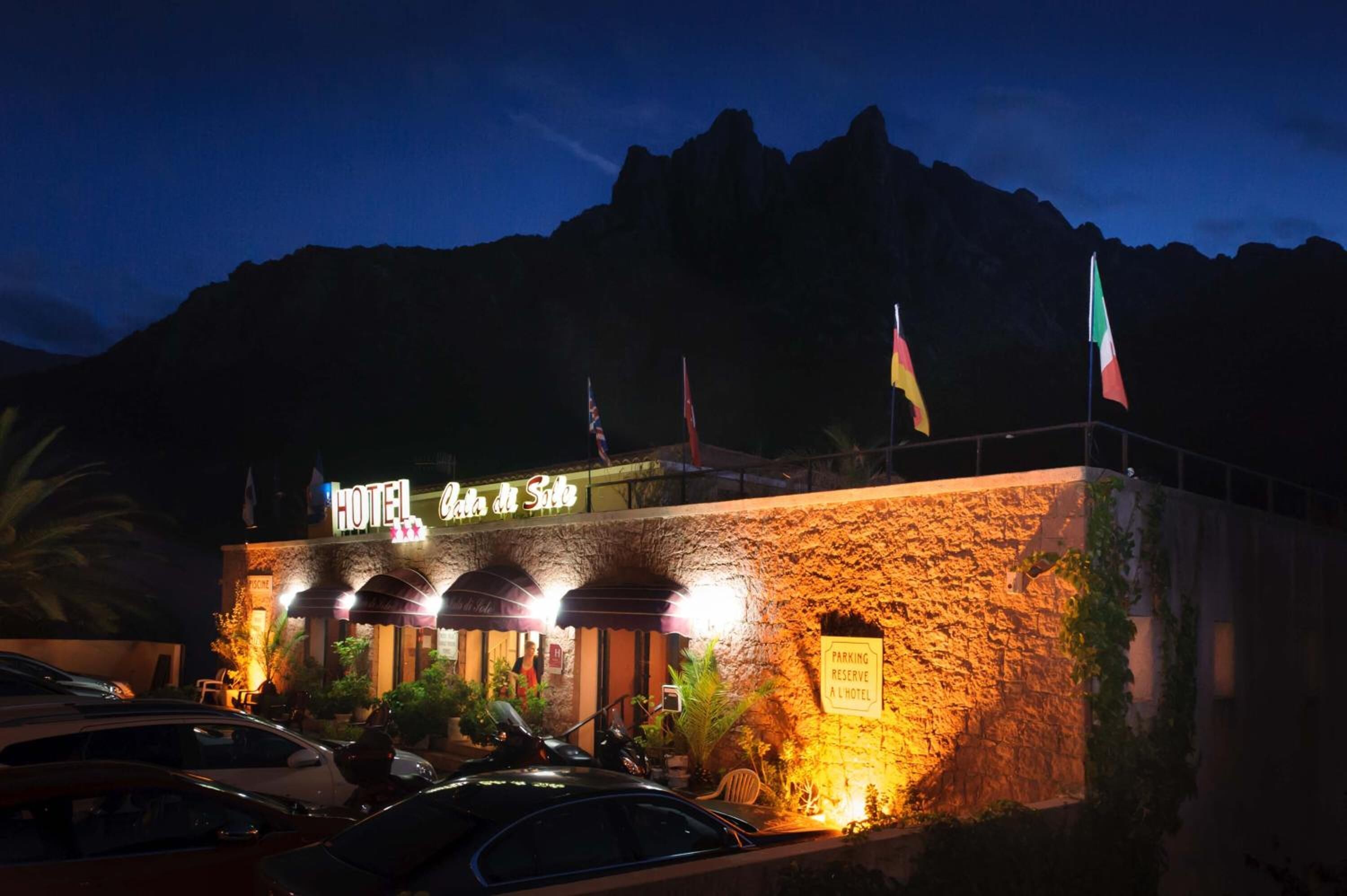 A hotel with a stone facade, illuminated signage, and flags.