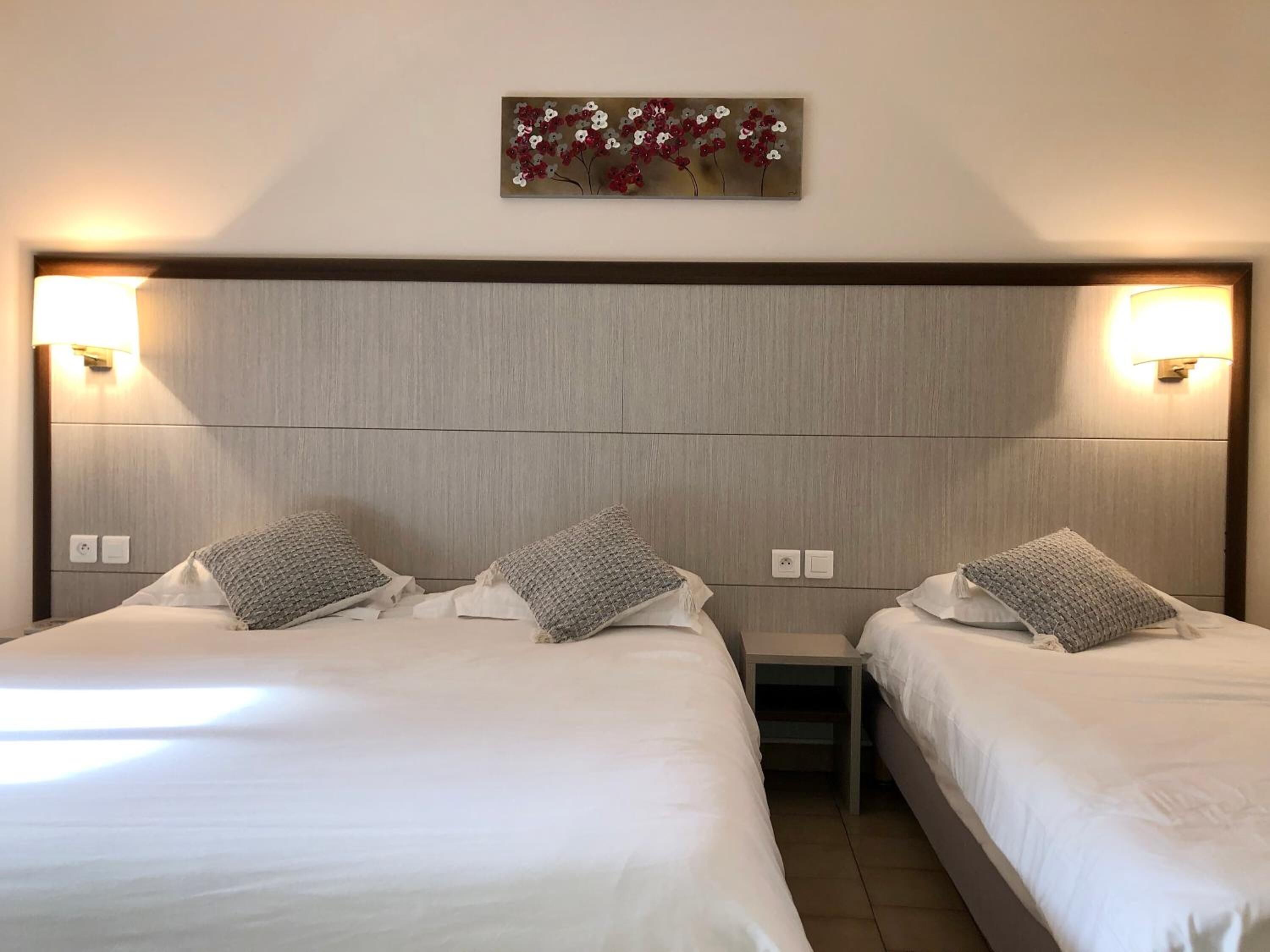 Une chambre d’hôtel avec deux lits, chacun étant équipé d’un oreiller et d’une table de chevet. Un luminaire est fixé au mur au-dessus des lits.