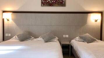 A hotel room with two beds, each with a pillow and a nightstand. There is a wall-mounted light fixture above the beds.