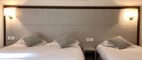 A hotel room with two beds, each with a pillow and a nightstand. There is a wall-mounted light fixture above the beds.