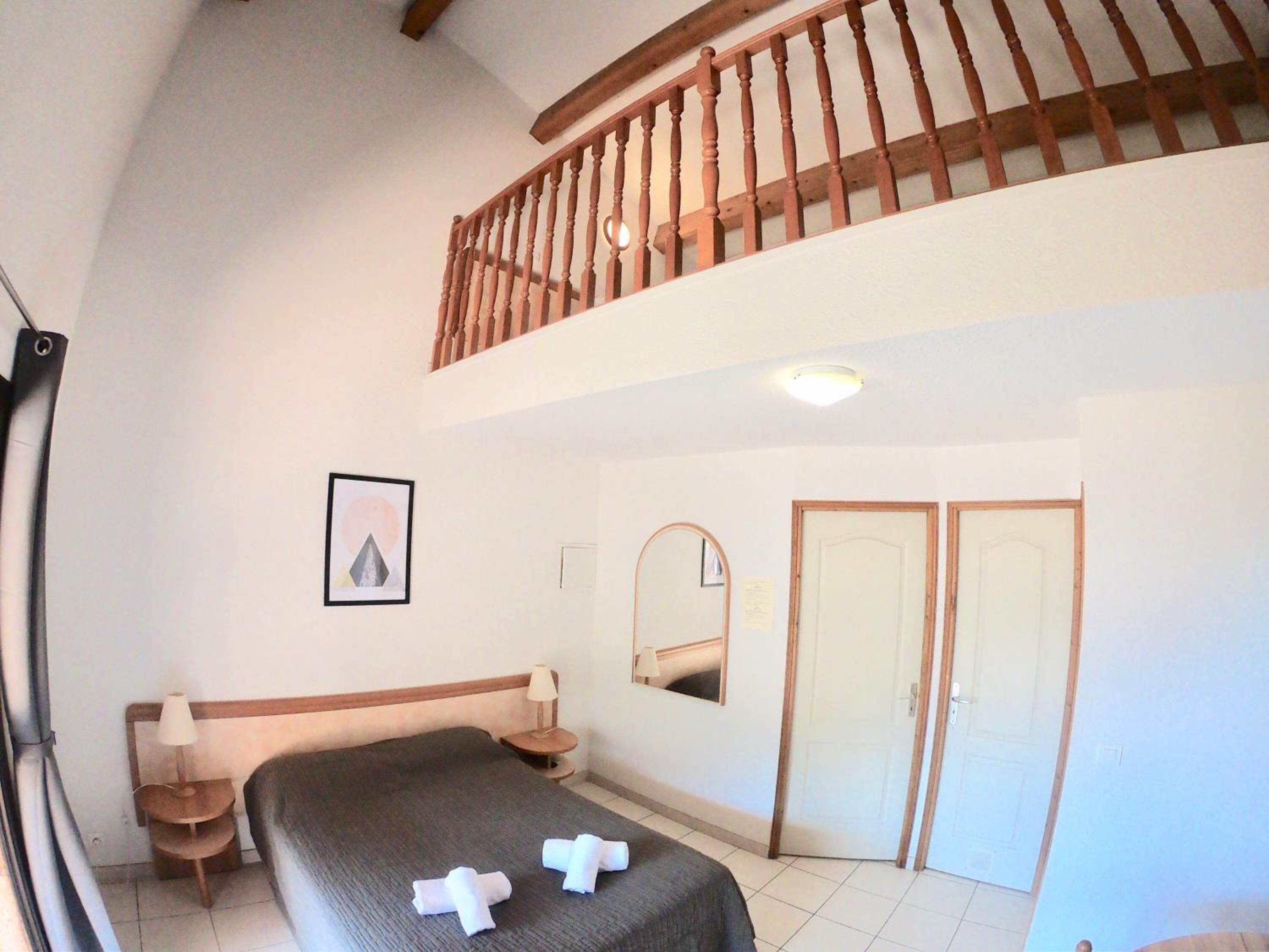 A bedroom with a bed, a nightstand, a lamp, a mirror, and a door.