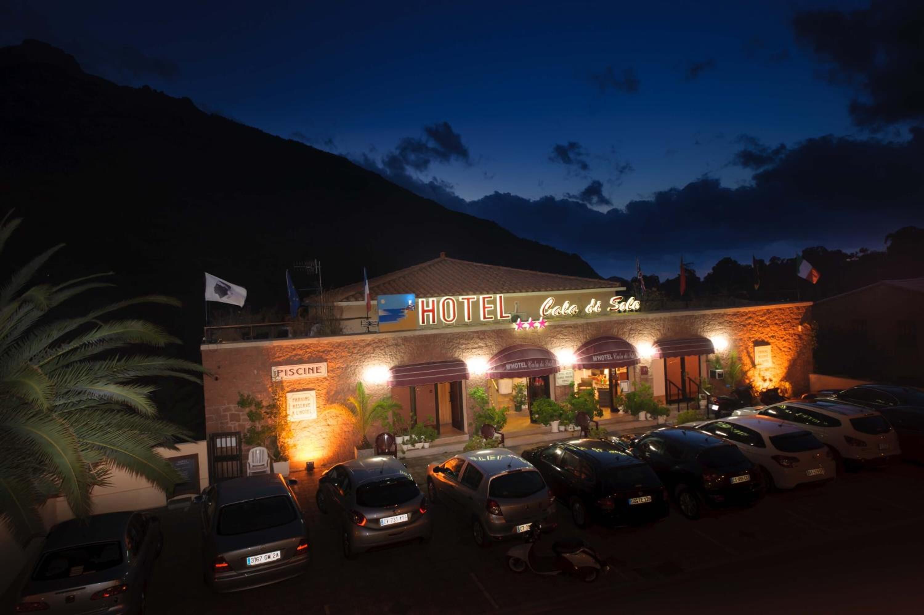 Een hotel met een bord waarop 'HOTEL Casa de Sol' staat en een parkeerplaats met verschillende auto's.