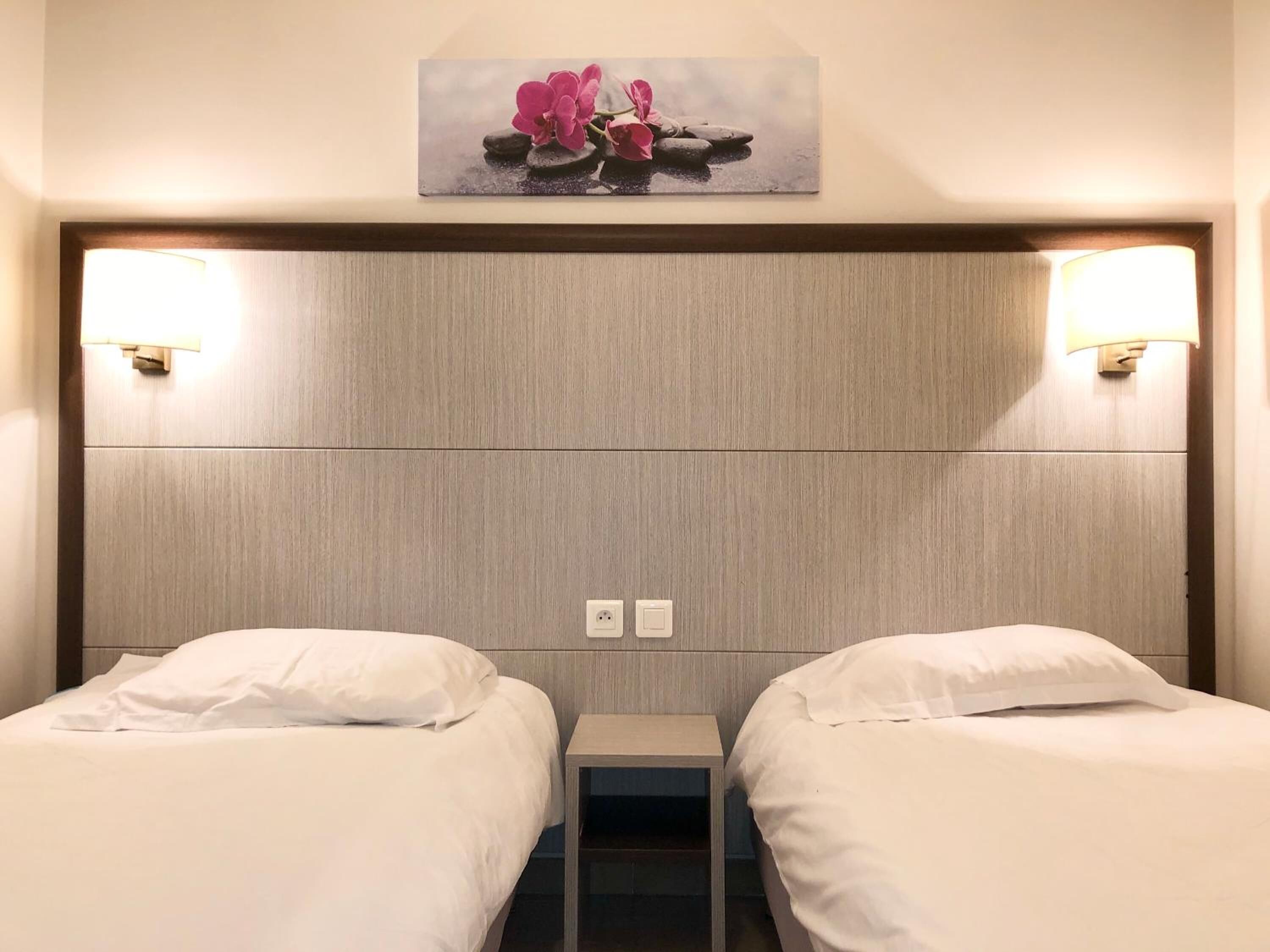 Habitación de hotel con dos camas, cabecera con luces de pared y un cuadro sobre las camas.