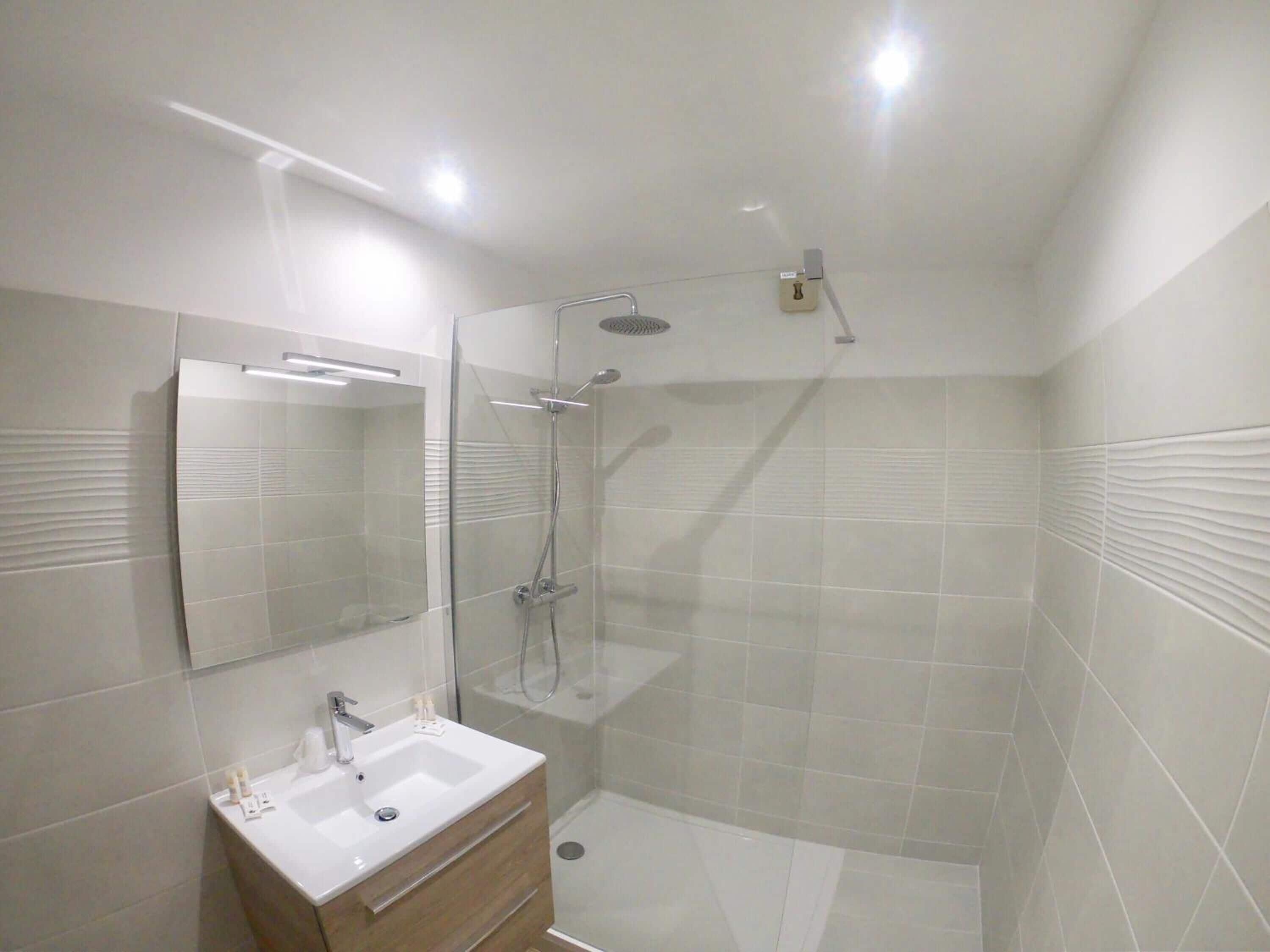 Un baño moderno con ducha envuelta en cristal, tocador con lavabo y un espejo grande.