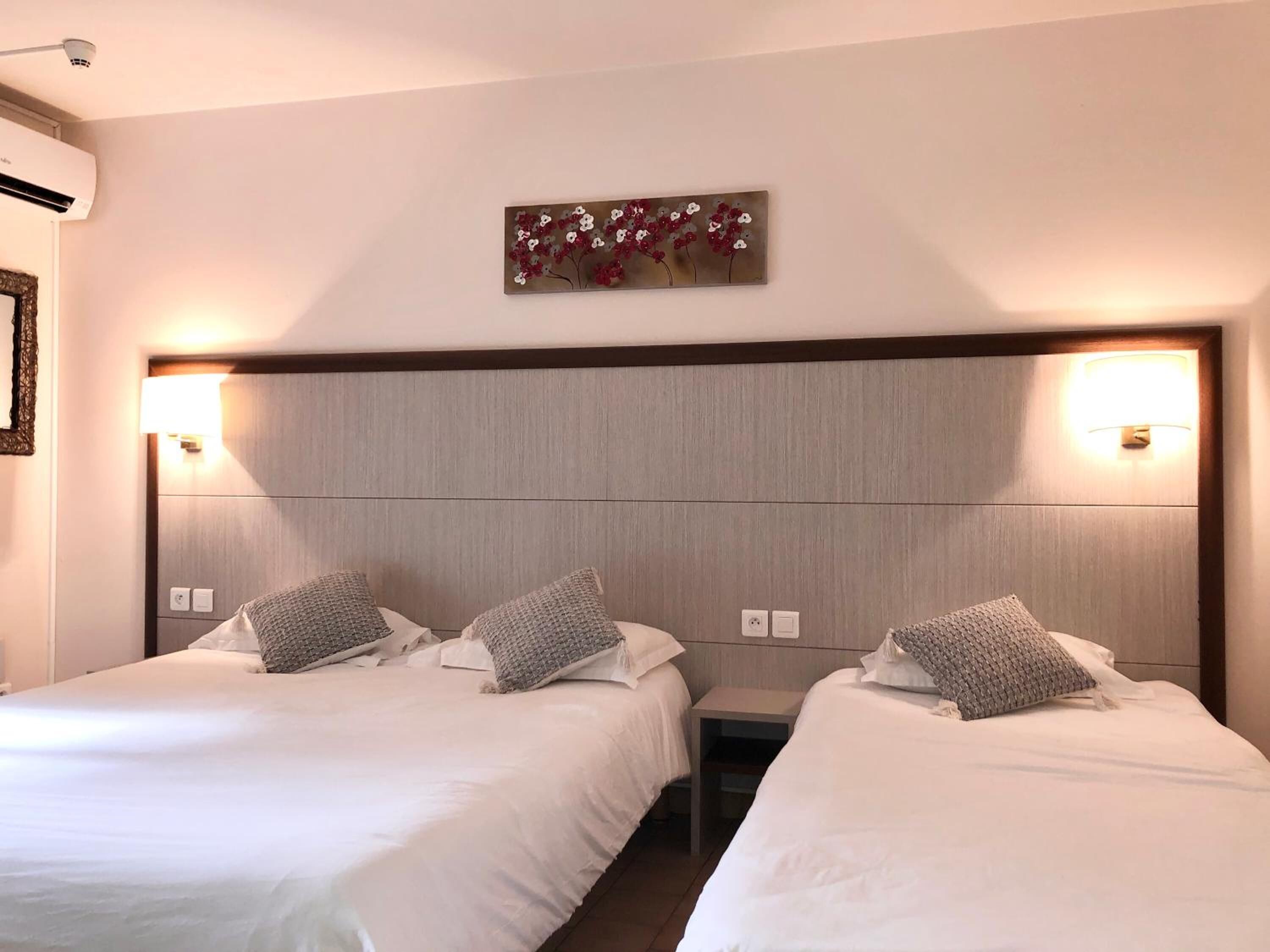 Habitación de hotel con dos camas, cada una con cabecera y lámparas de noche.