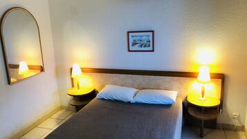 Una camera d'albergo con un letto, due lampade da comodino, un tavolino di appoggio, un quadro appeso alla parete e uno specchio.