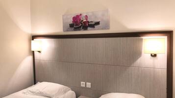 A hotel room with two beds, a nightstand, and a wall-mounted picture of pink flowers.