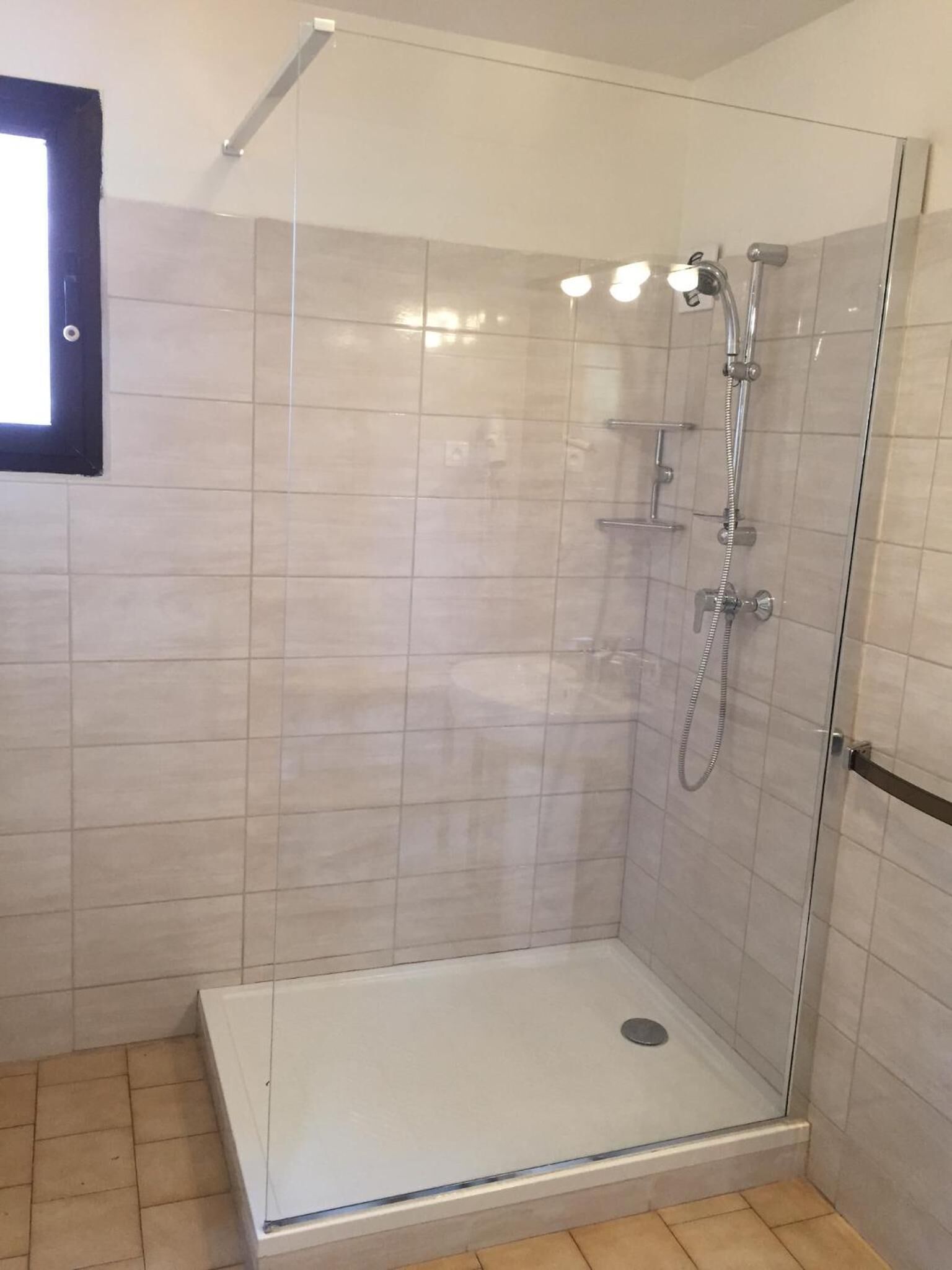 A glass-enclosed shower stall with a tiled floor, a visible drain, and a showerhead.