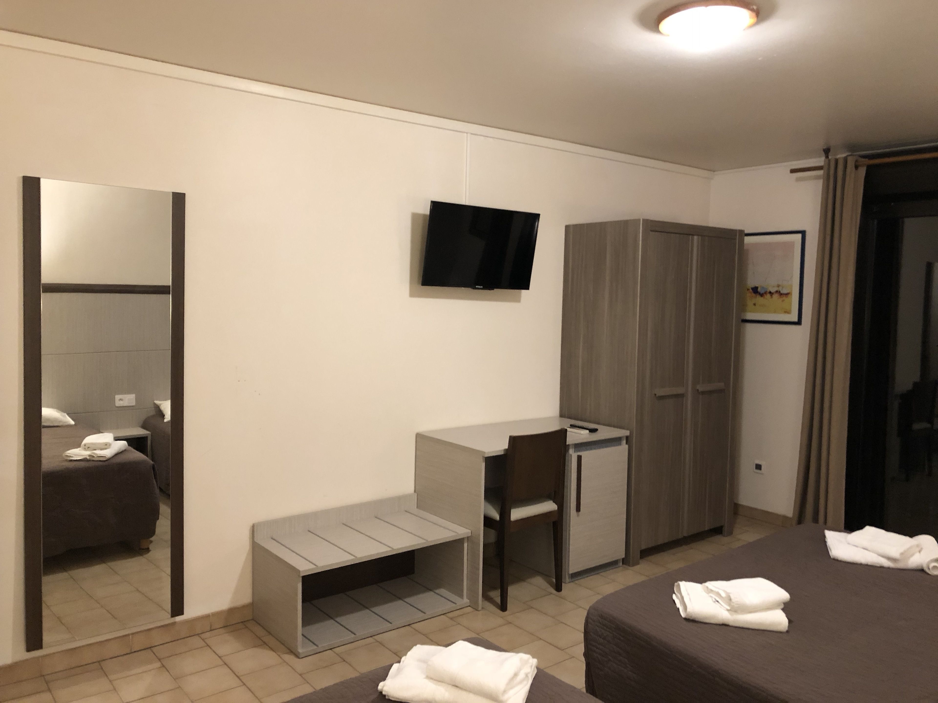 Habitación de hotel con cama, escritorio, silla, armario y televisor montado en la pared.