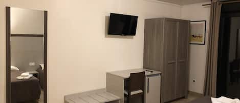 Habitación de hotel con cama, escritorio, silla, armario y televisor montado en la pared.