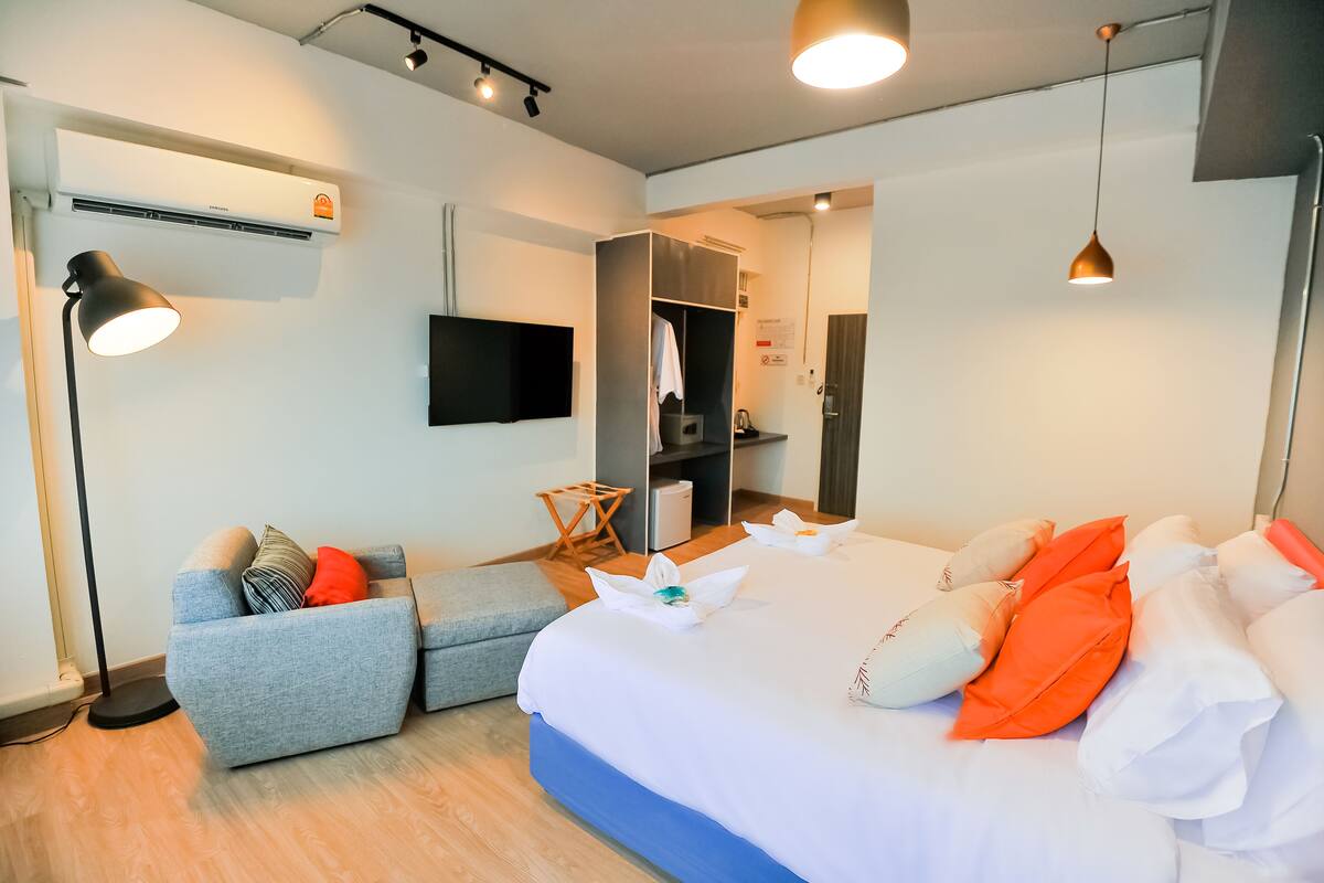 A modern hotel room with a bed, a sofa, a desk, and a flat-screen TV.