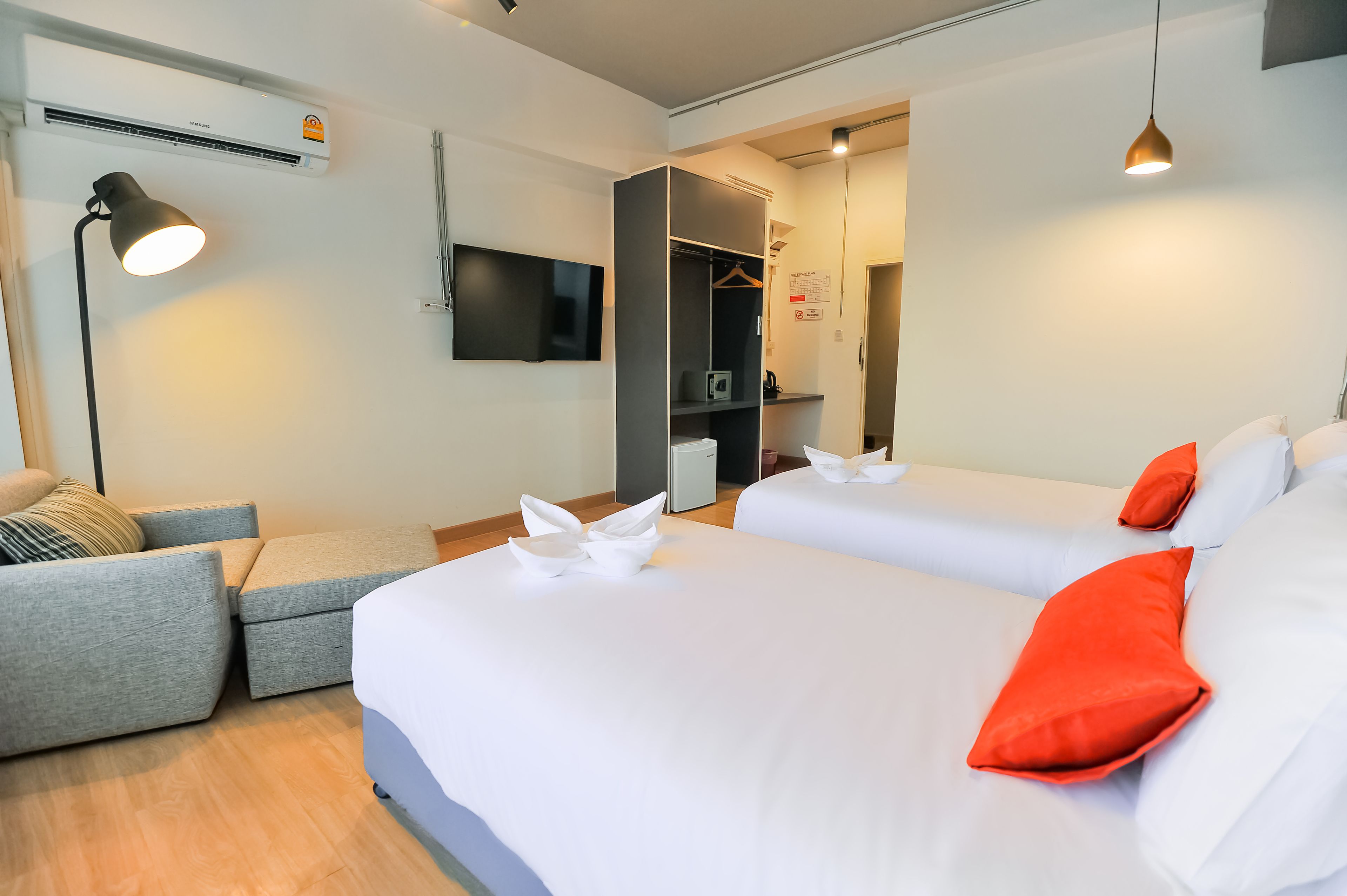 A hotel room with two beds, a grey sofa, a desk, and a wardrobe.